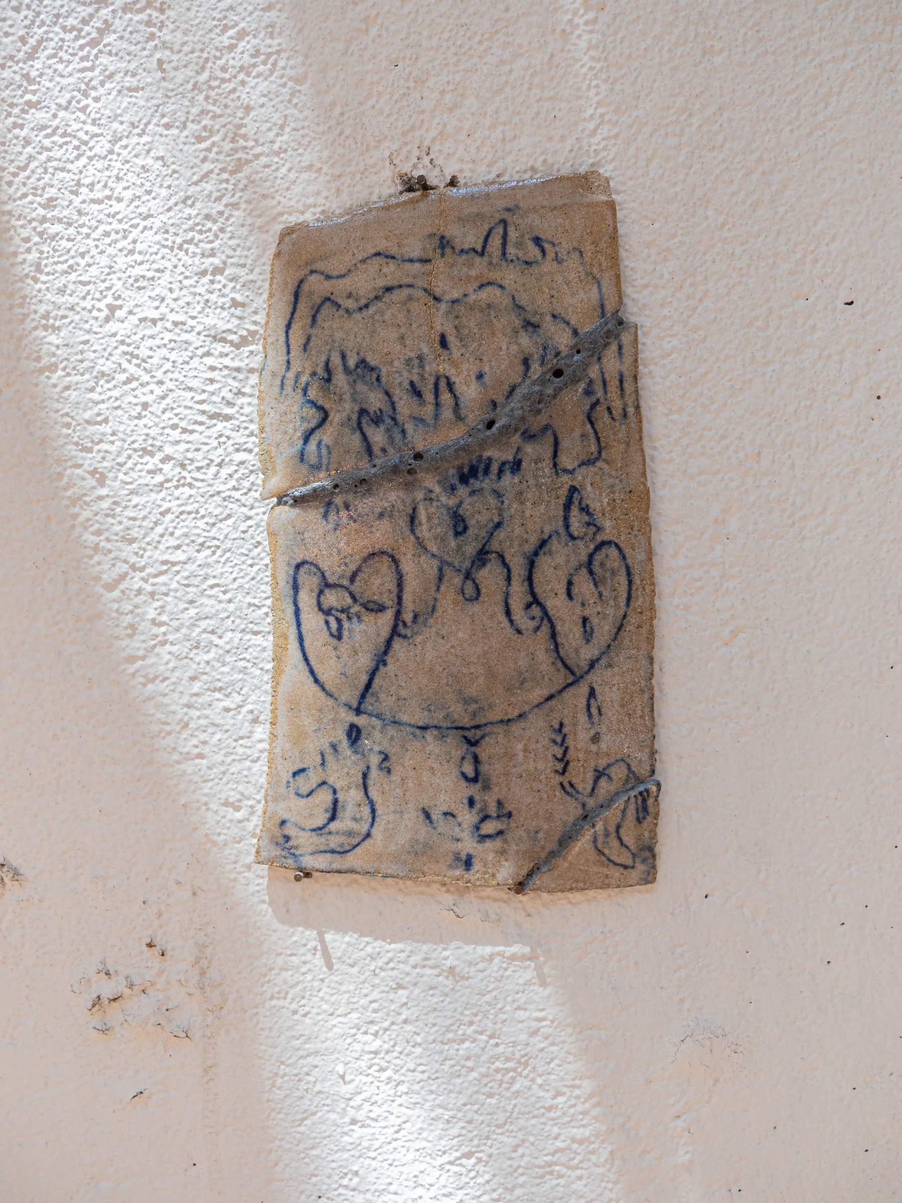Placa cerámica rectangular con trazos azules sobre pared blanca